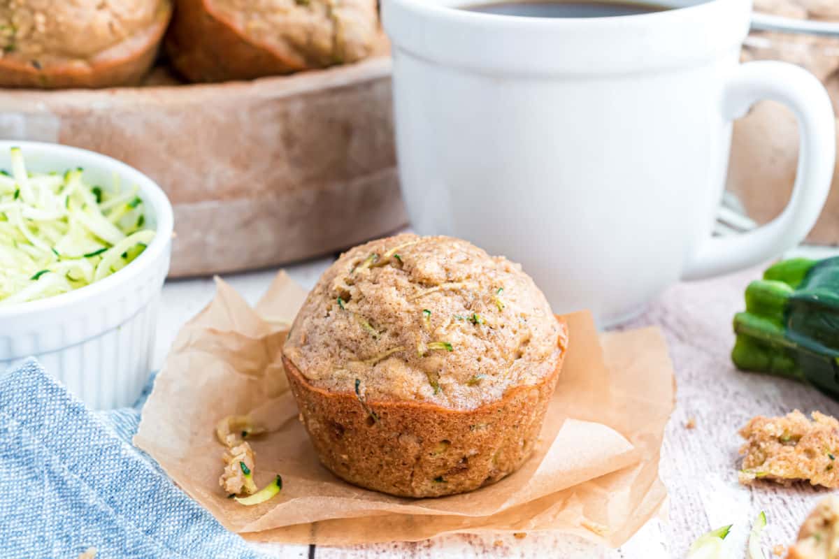 Zucchini muffin on a piece of parchment paper with mug of coffee.
