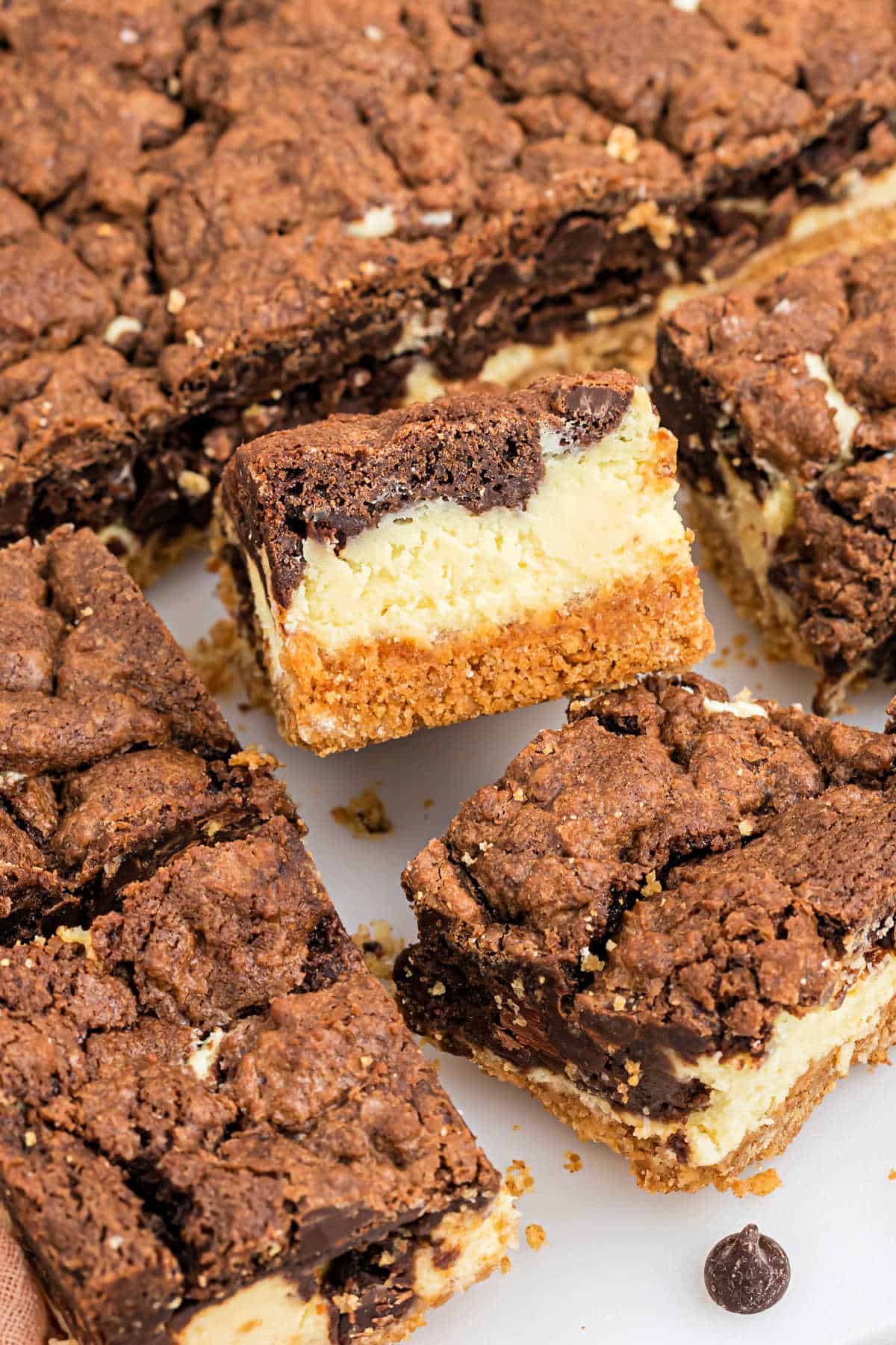 Chocolate cheesecake bars with a crumbly crust, layered with rich chocolate and creamy cheesecake, cut into squares on a white surface.