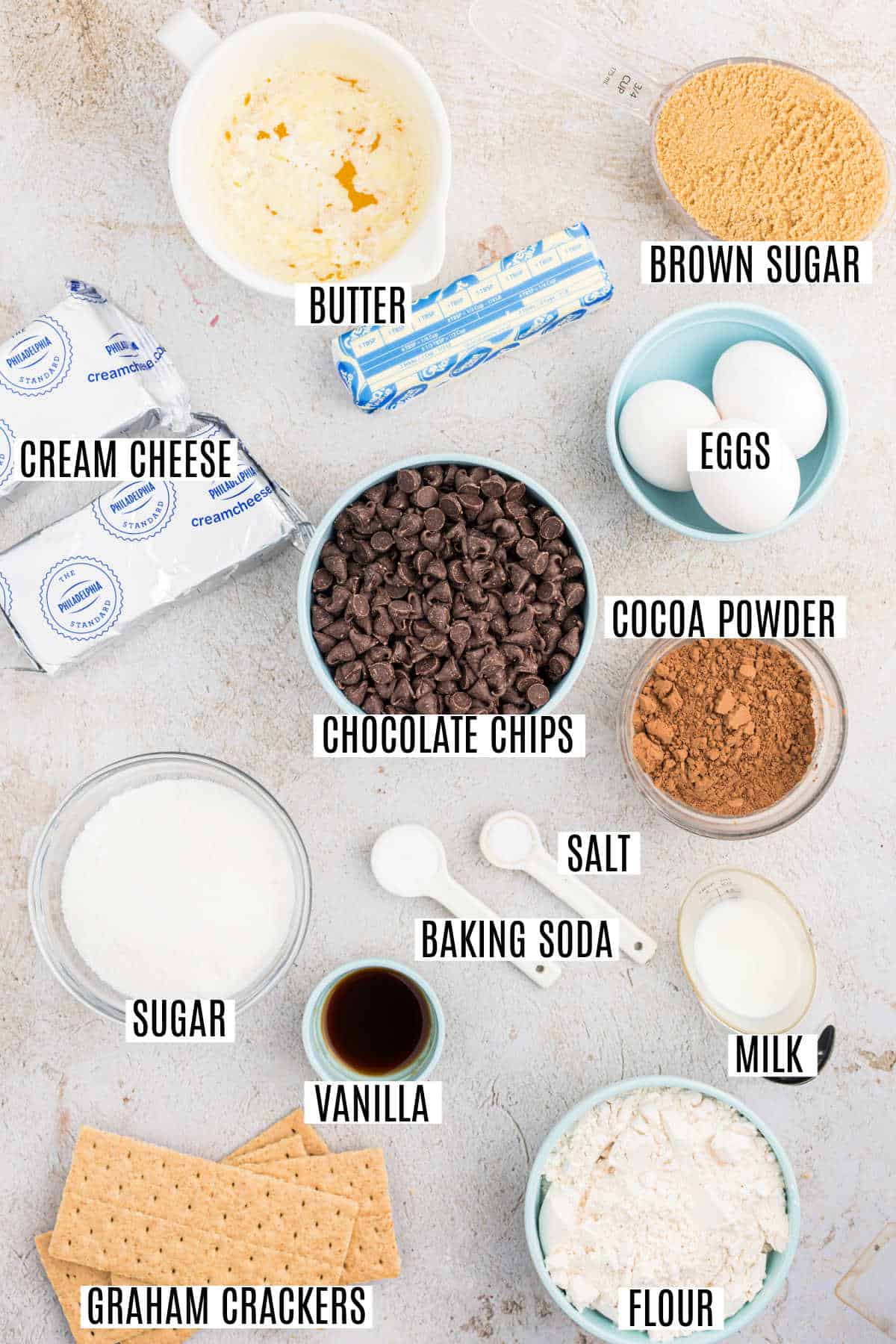 Baking ingredients labeled on a counter: butter, brown sugar, eggs, cocoa powder, chocolate chips, and more—everything you need to whip up decadent chocolate cheesecake bars.