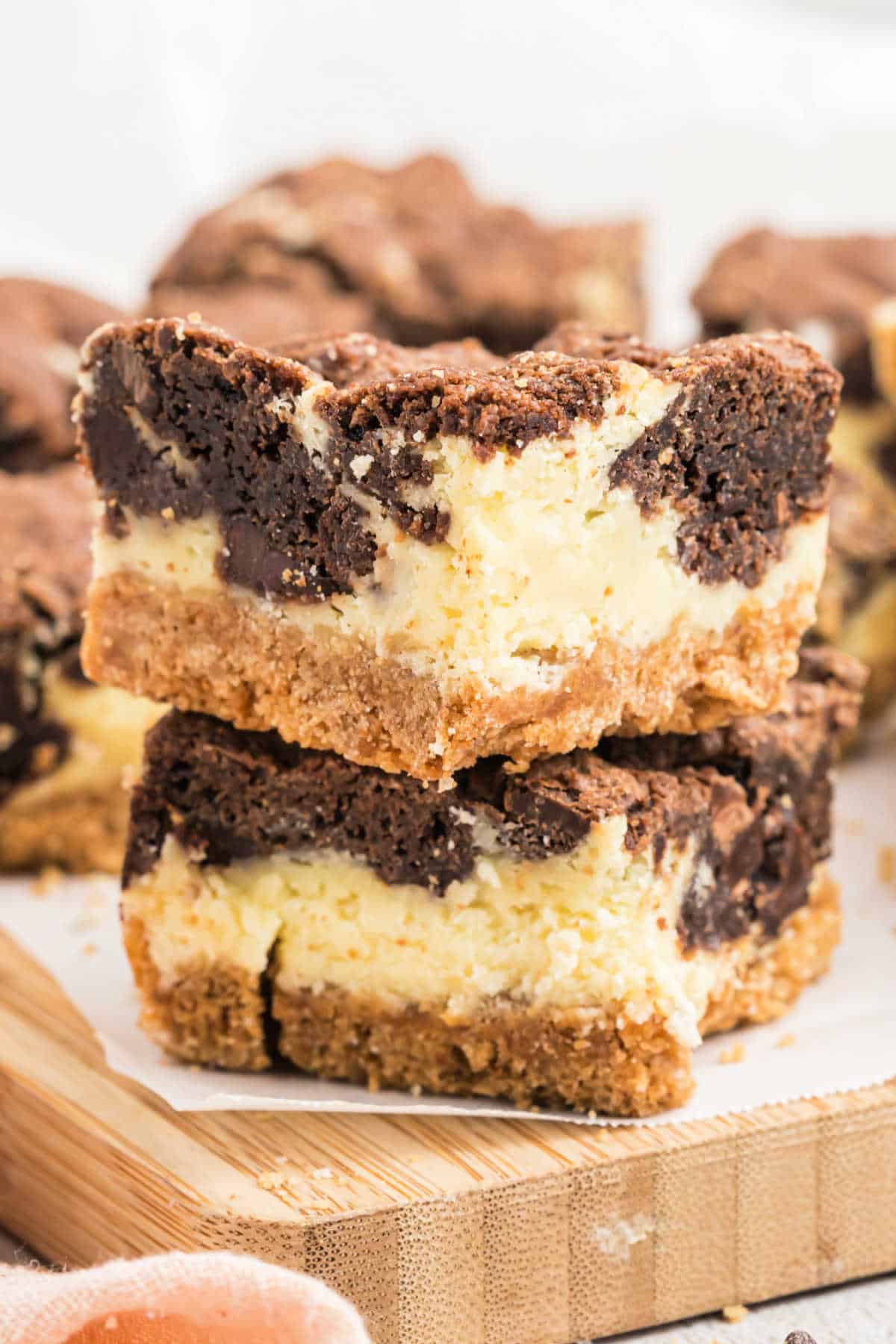 Two chocolate cheesecake bars are stacked on a wooden board, showcasing their creamy and chocolate layers.