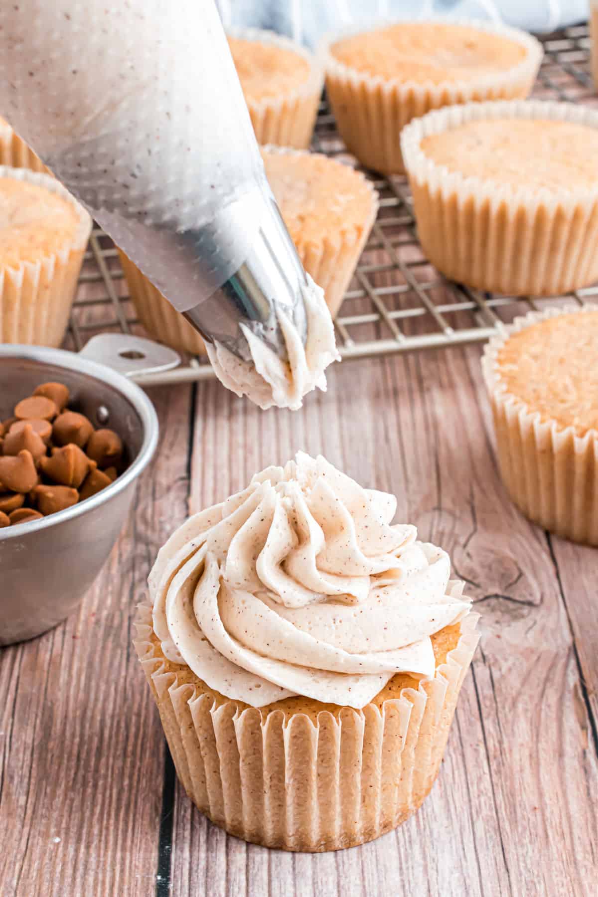 Cinnamon frosting being piped onto spice cupcakes.
