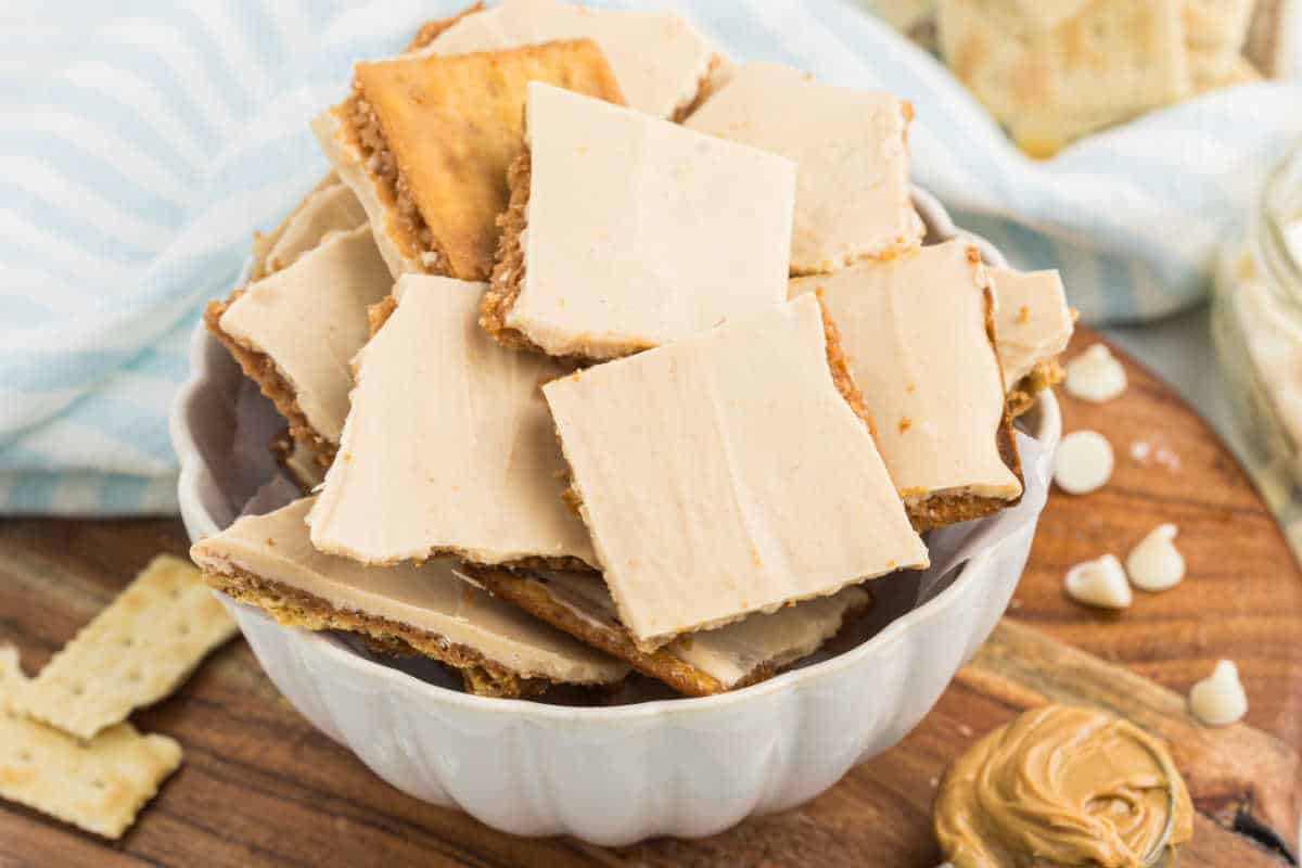 A bowl filled with peanut butter cracker toffee bars, topped with a creamy frosting, sits on a wooden surface.