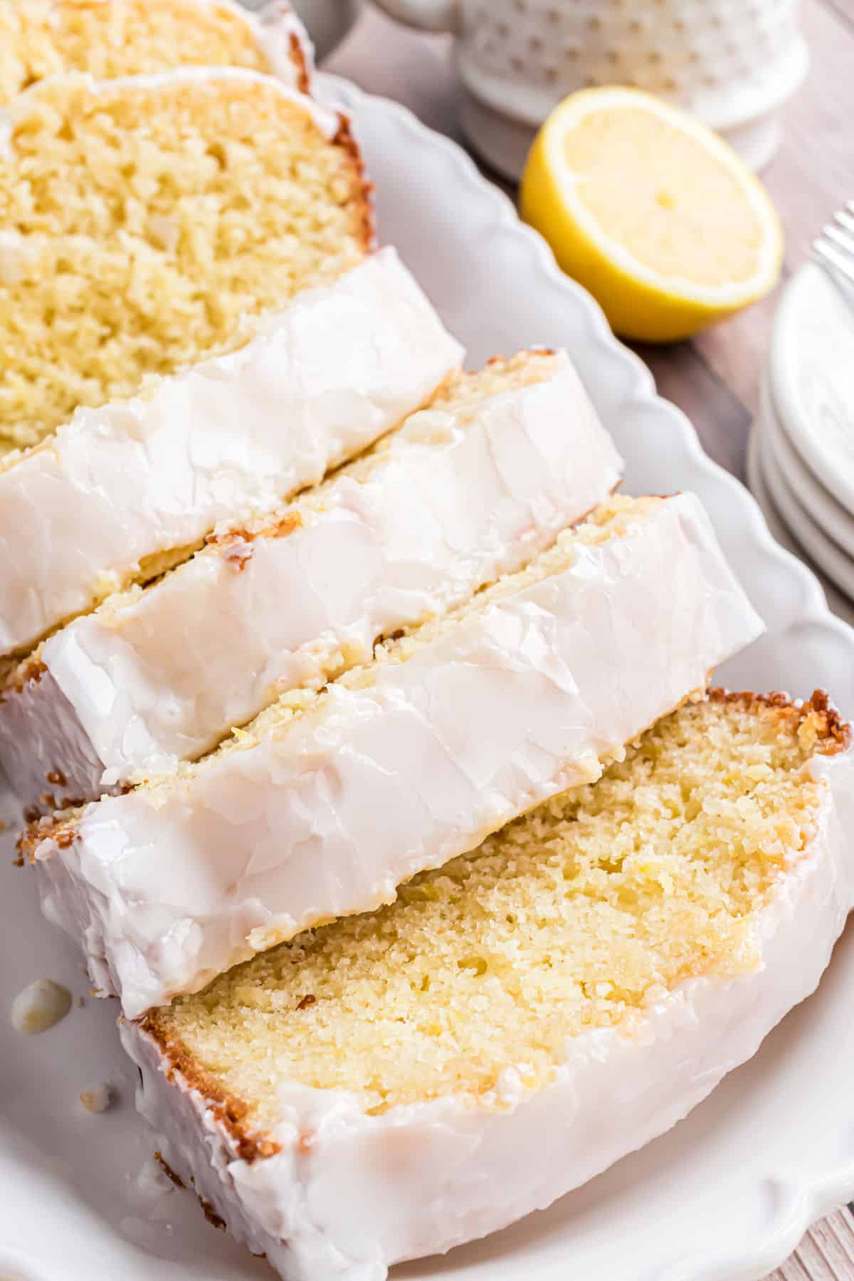 Loaf of lemon bread with icing sliced on a white serving plate.