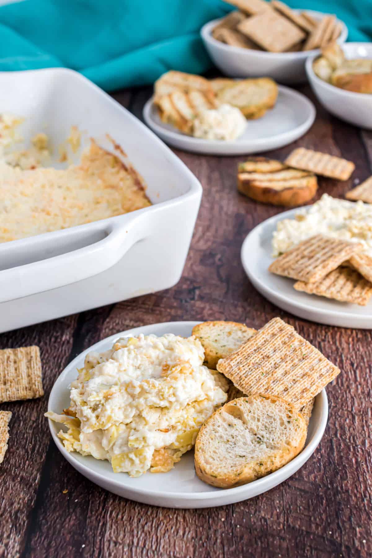 Artichoke dip served on a plate with triscuits and hearty bread pieces.