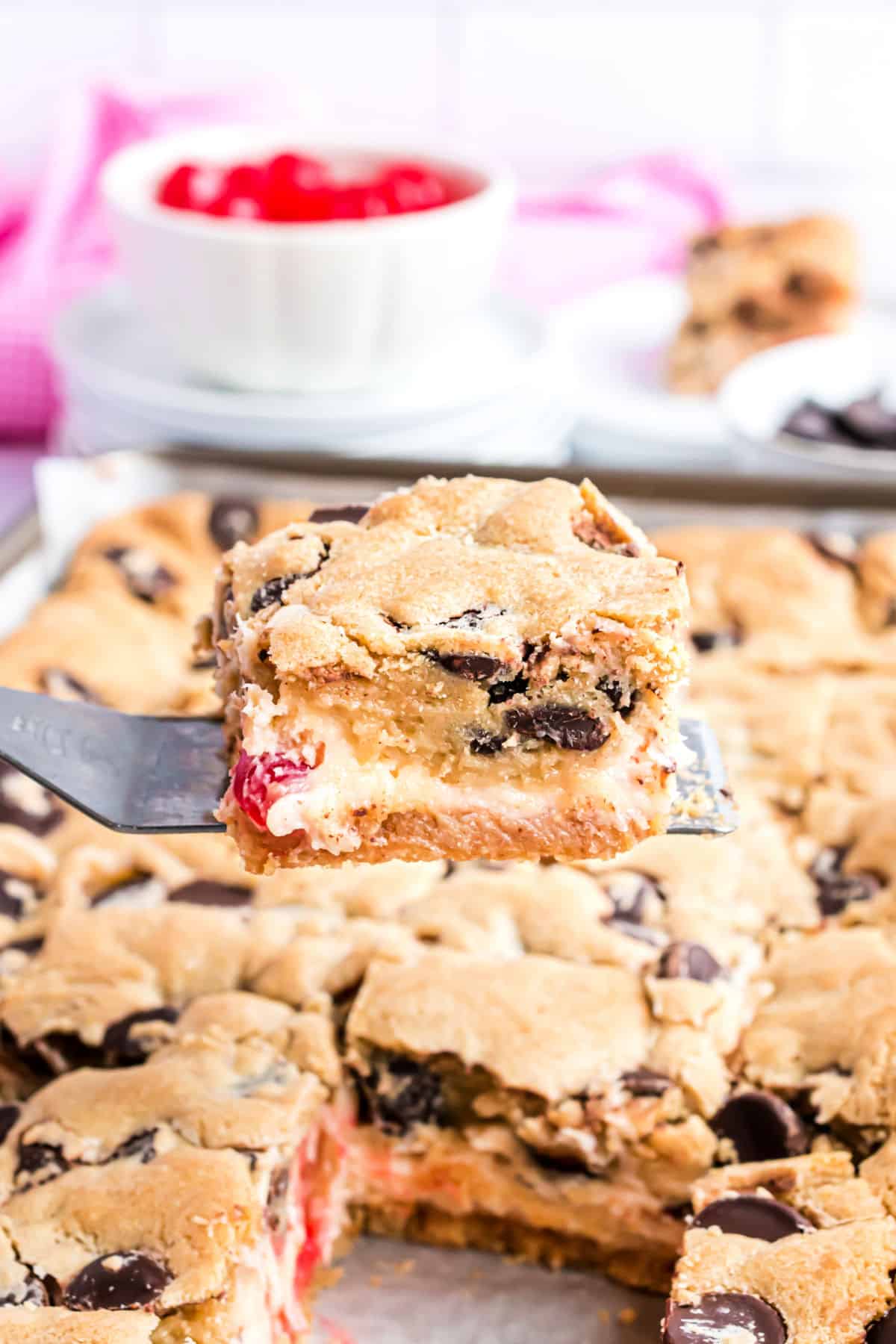 Cherry chocolate chip cheesecake bars being served with a spatula.