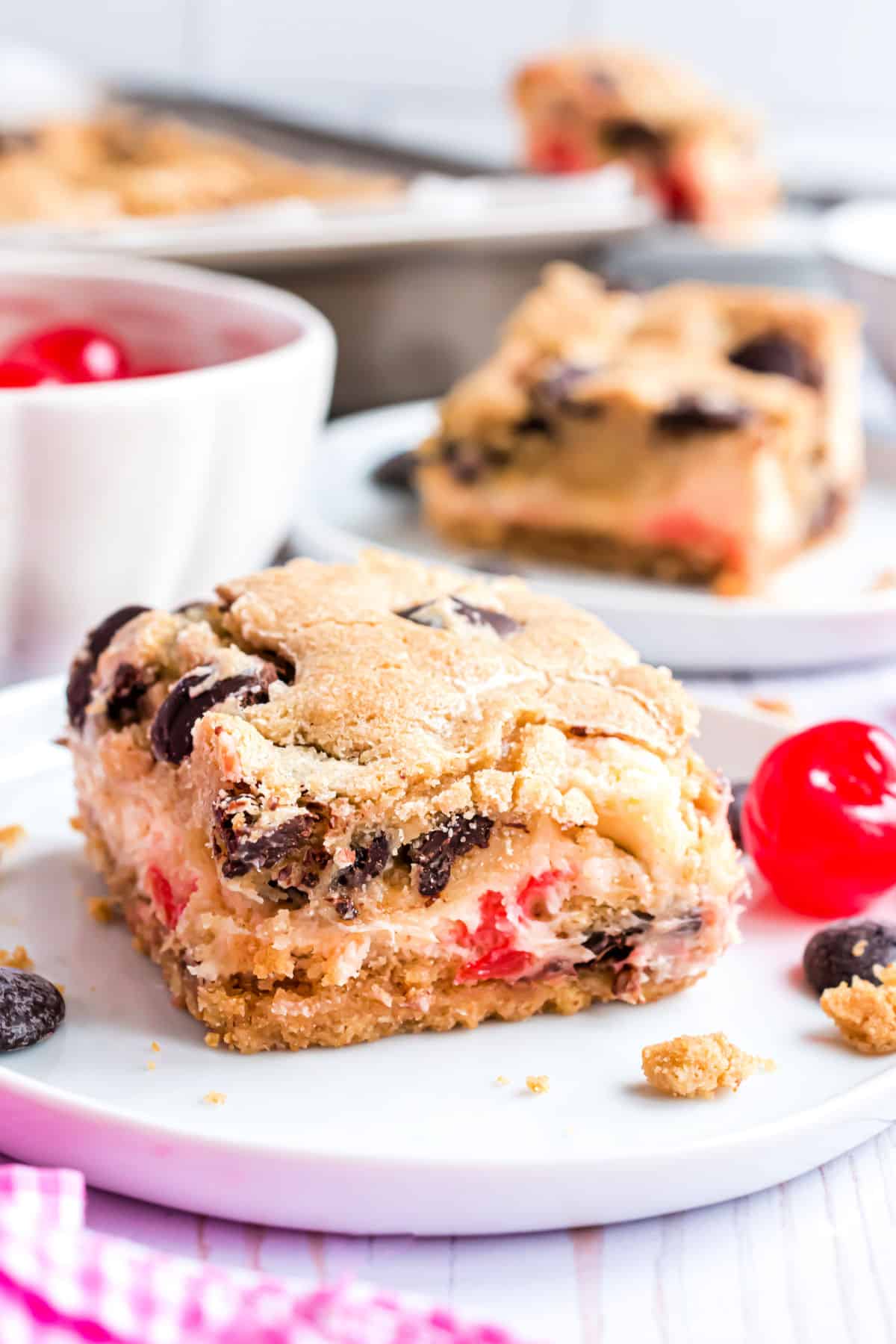 Chocolate chip cookie bars with a cherry cheesecake filling on a white plate.