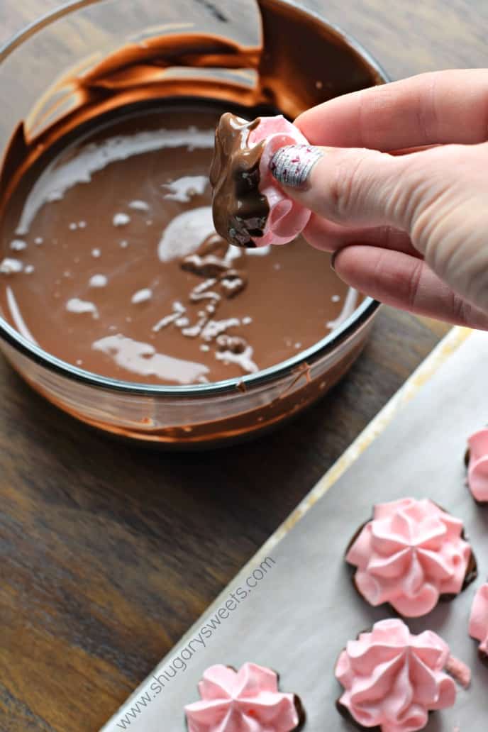 Strawberry meringue cookie being dipped in melted chocolate.