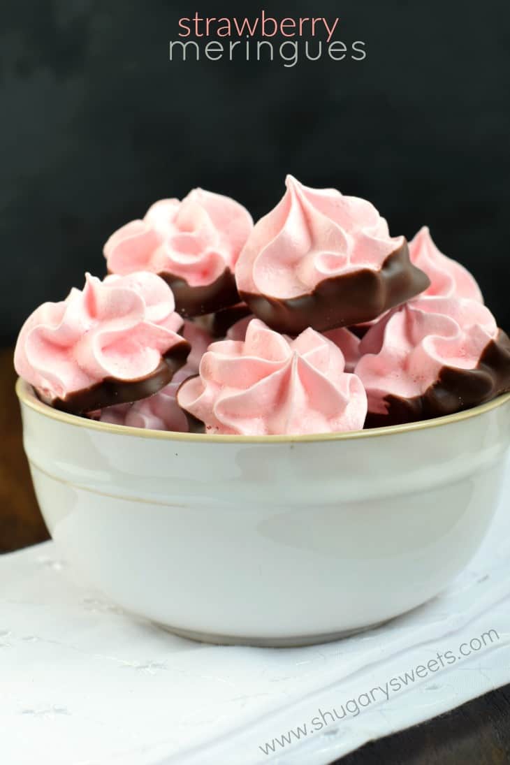 Off white bowl filled with chocolate dipped strawberry meringue cookies.