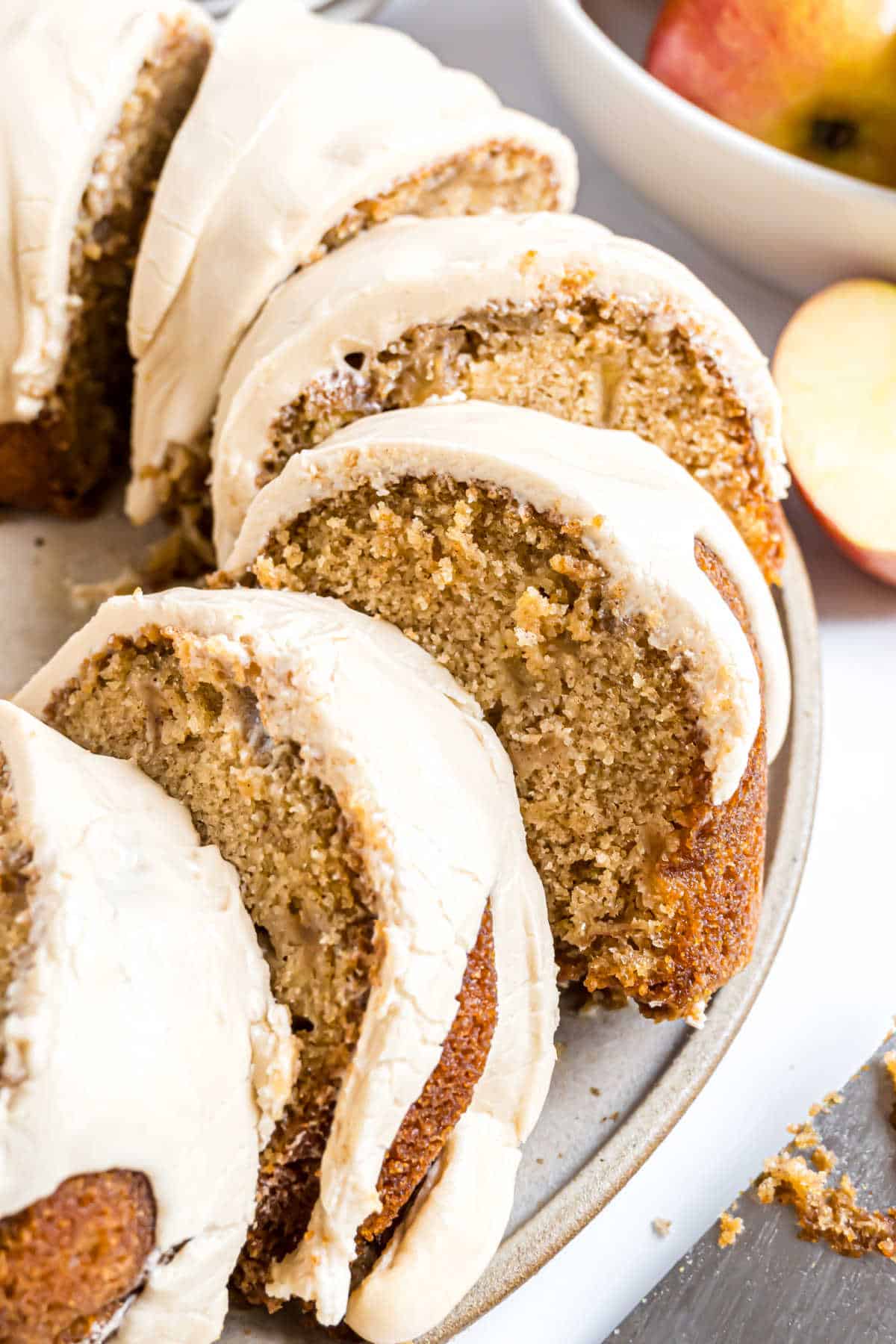 Sliced caramel apple bundt cake with white icing on a plate, with apples in the background.
