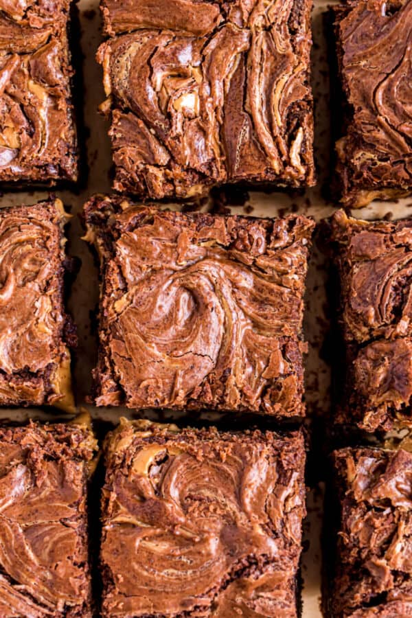 Squares of peanut butter swirled brownies on a parchment paper baking sheet.