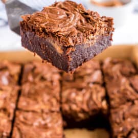 Peanut butter swirled brownies being lifted with a spatula out of baking pan.