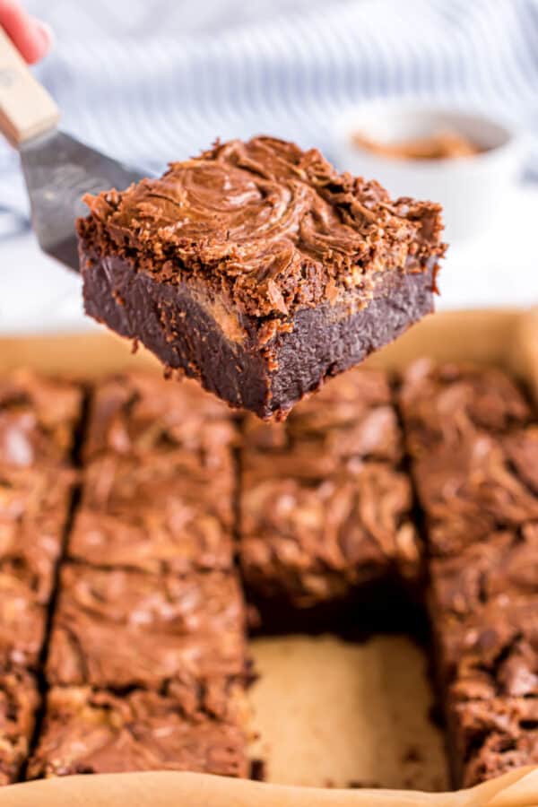 Peanut butter swirled brownies being lifted with a spatula out of baking pan.