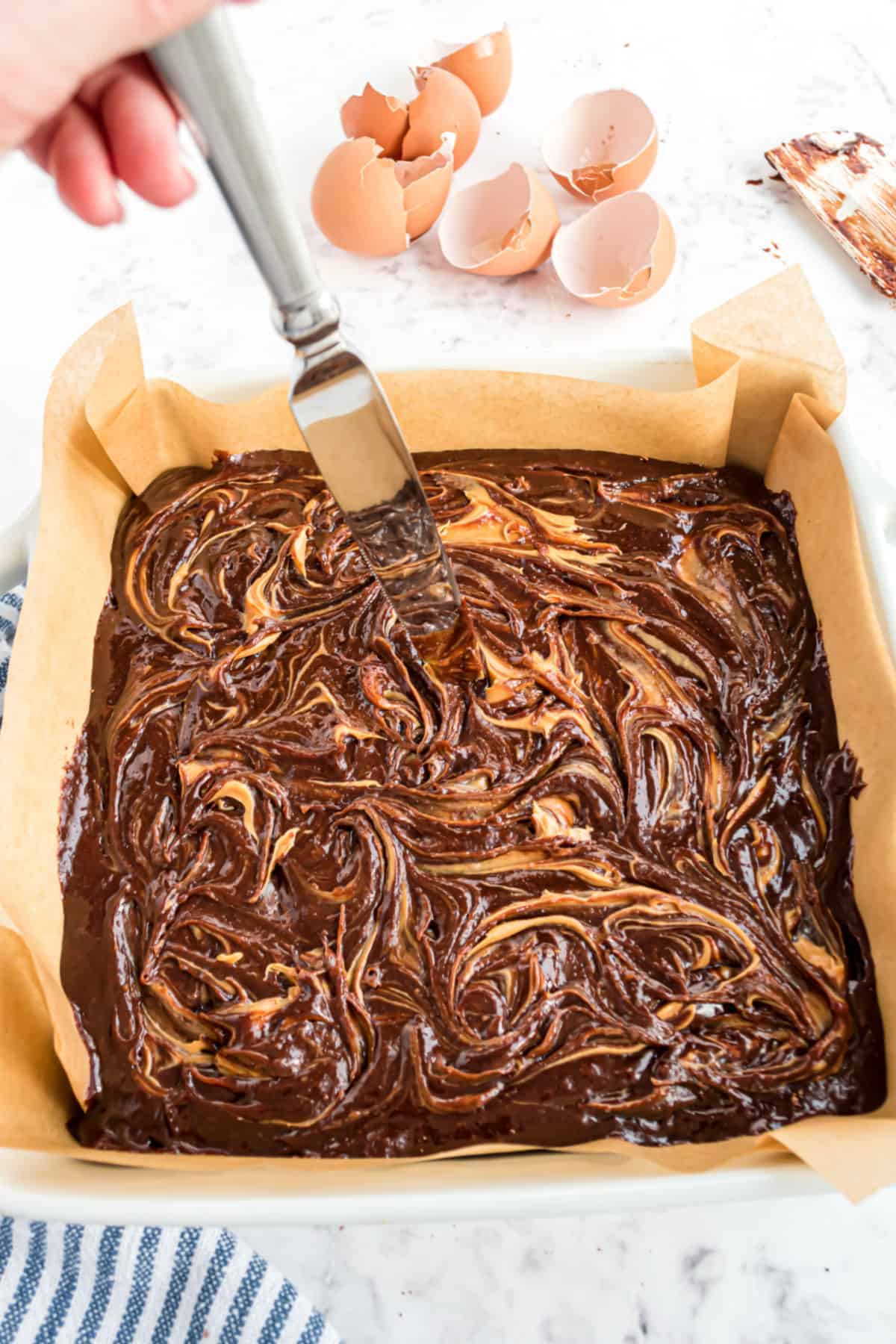 Peanut butter swirled into brownie batter with a knife.
