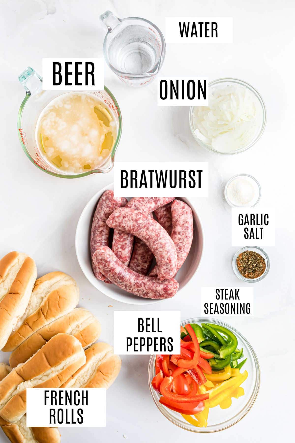 Top-down view of slow cooker beer brats with sliced onions, bell peppers, garlic salt, steak seasoning, and French rolls.