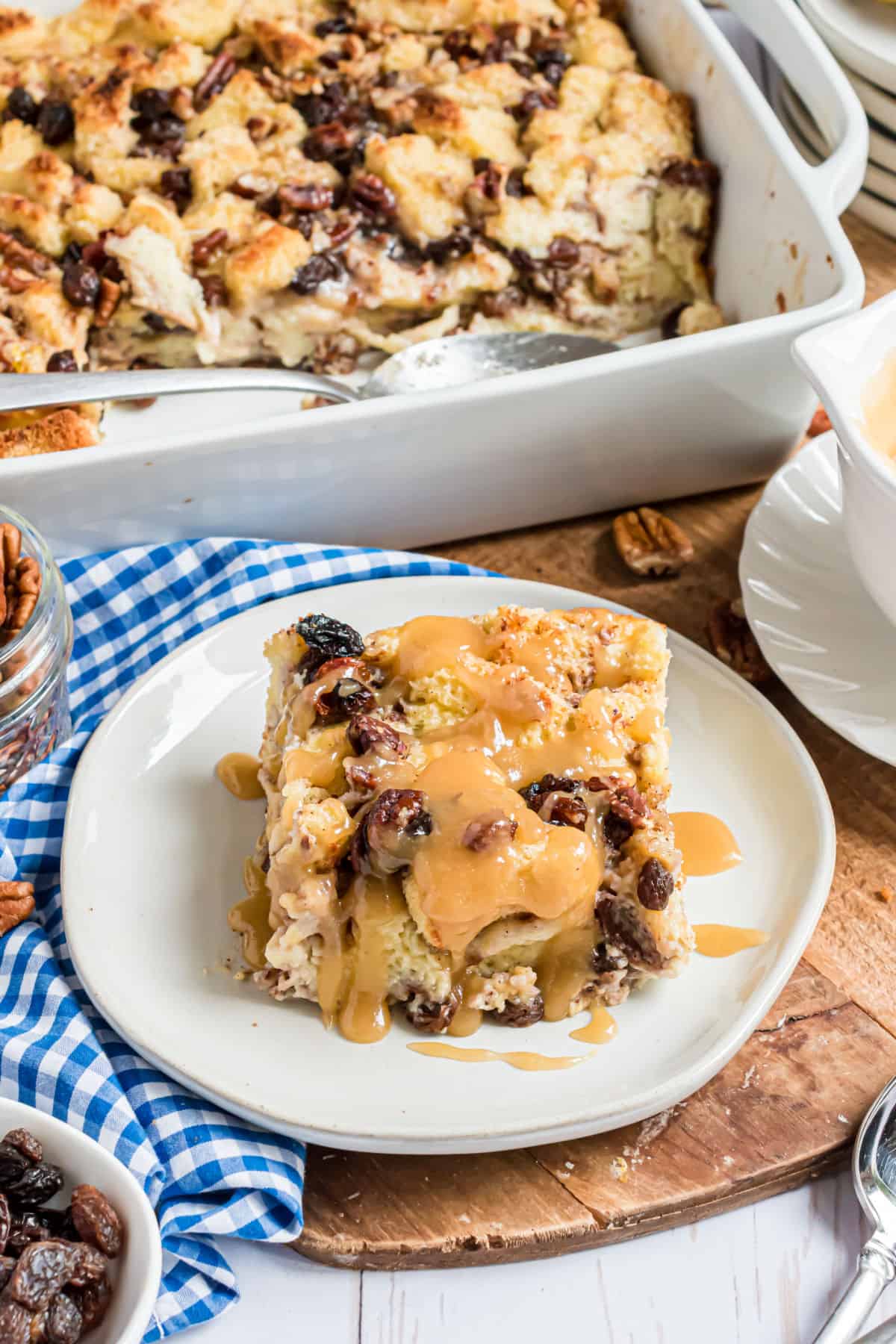 Slice of bread pudding with raisins served on a white plate with caramel sauce.