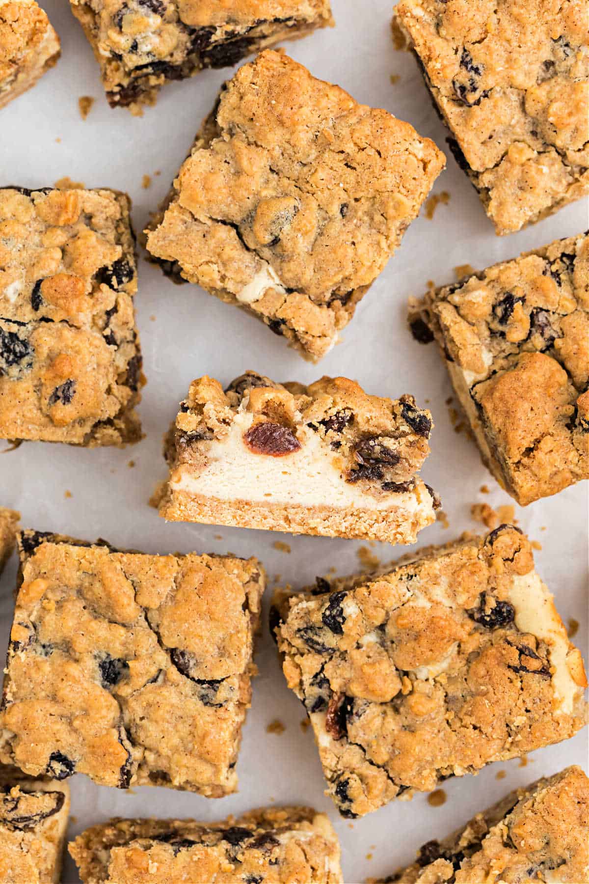 Oatmeal raisin cookie cheesecake bars with a creamy filling, arranged on a white surface, offer a delicious twist on the classic treat.