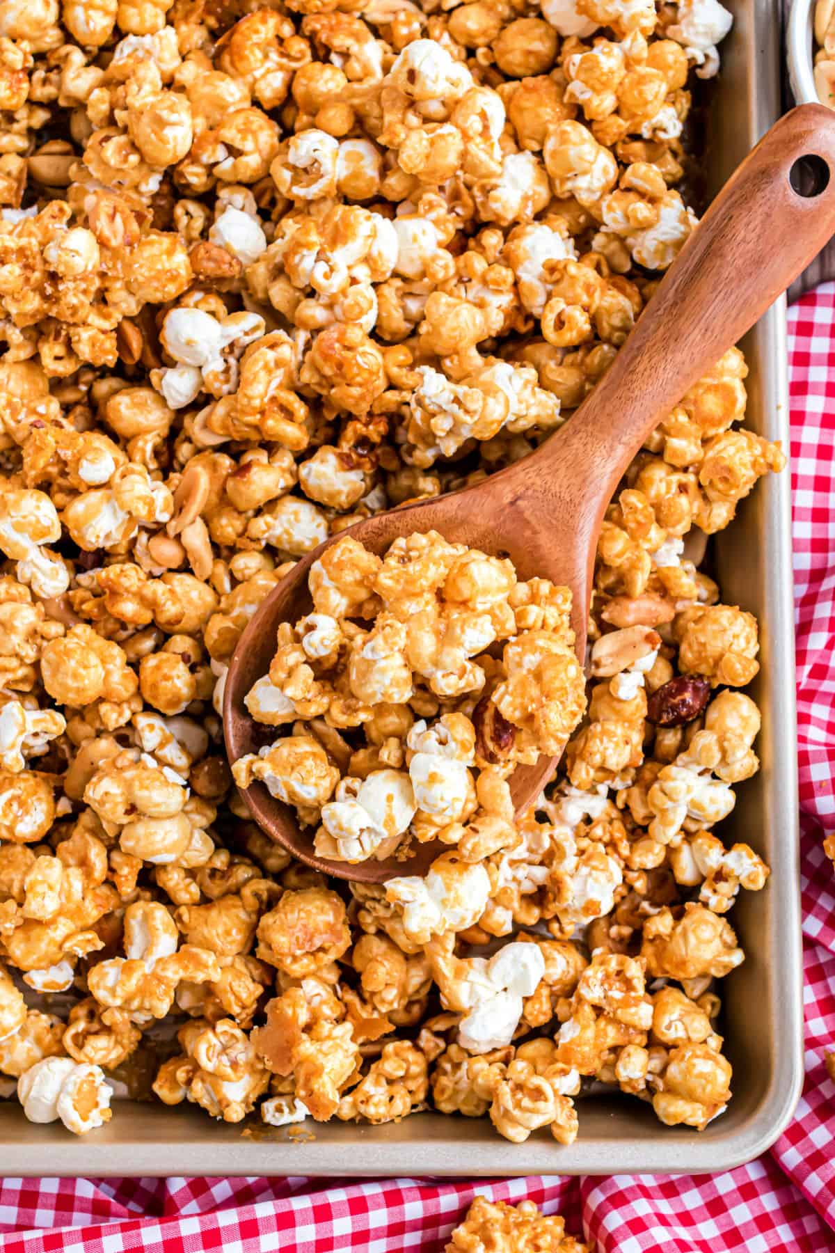 Caramel popcorn on cookie sheet with wooden spoon.