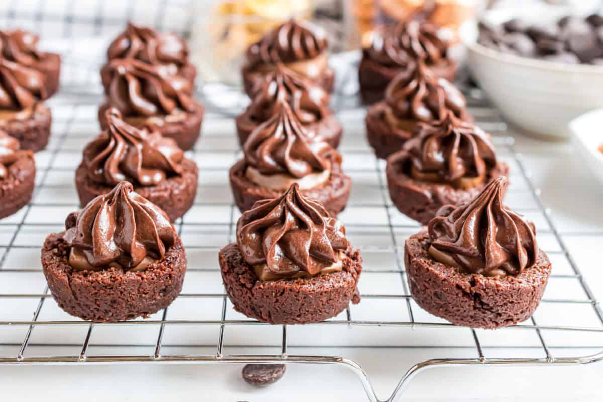Brownie bites with caramel and frosting on a wire rack.