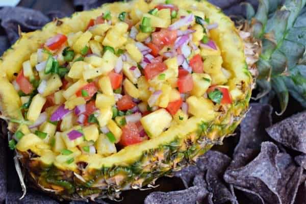 Pineapple salsa in a hollowed out pineapple with blue corn chip scoops.