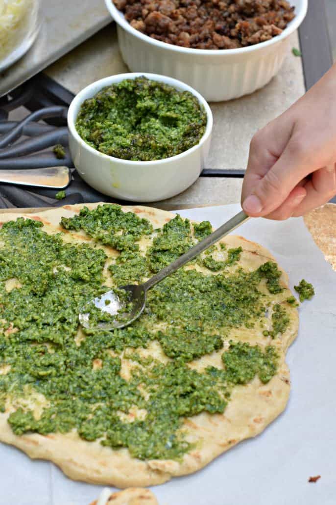 Homemade pesto being spread onto a pizza crust with a spoon.