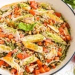 Spaghetti chicken pesto pasta topped with grilled chicken, diced tomatoes, pesto sauce, walnuts, and shredded parmesan in a white bowl.