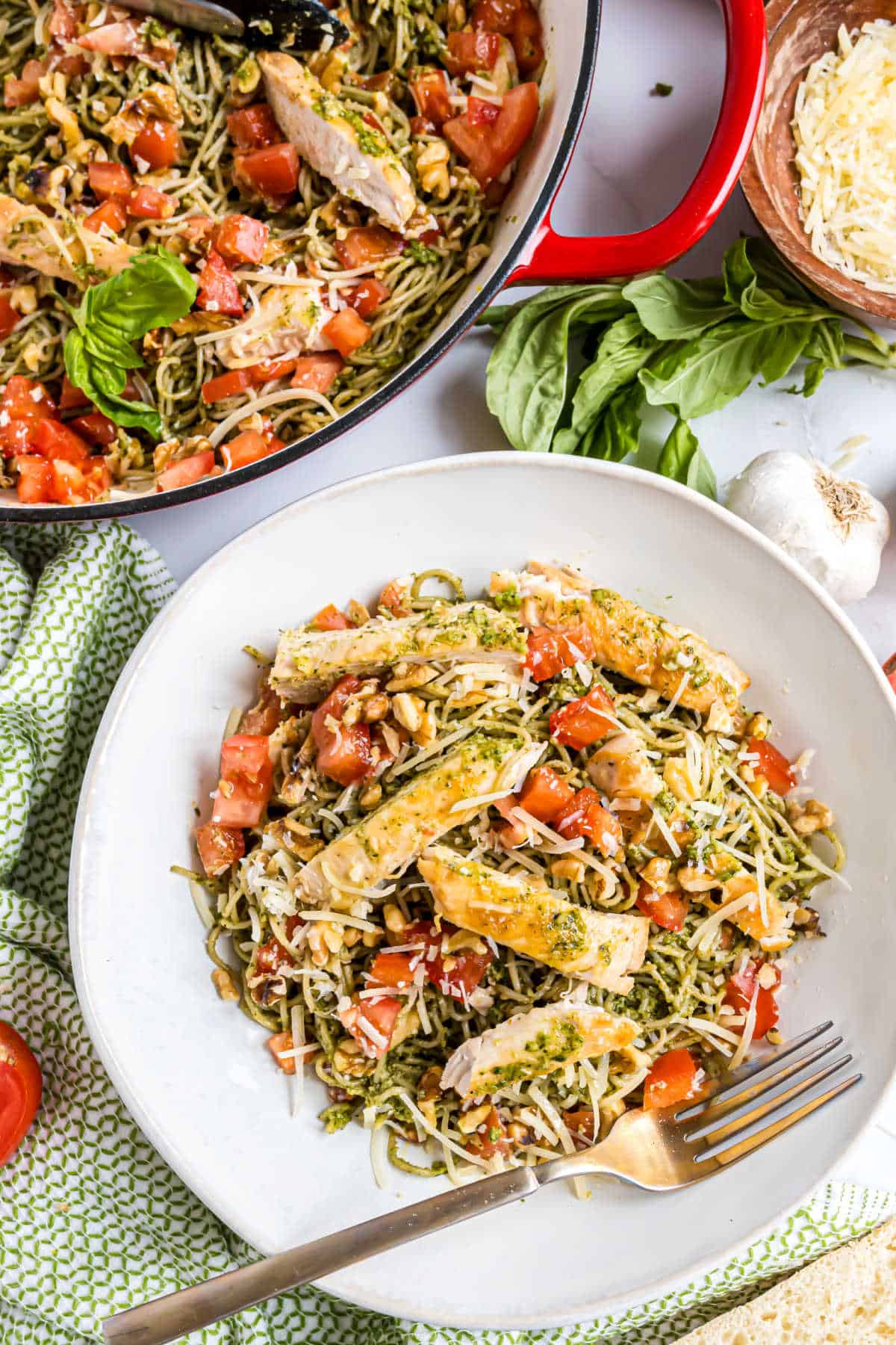 Plate of chicken pesto pasta with grilled chicken, diced tomatoes, and parmesan, served beside a pot filled with the same flavorful dish.