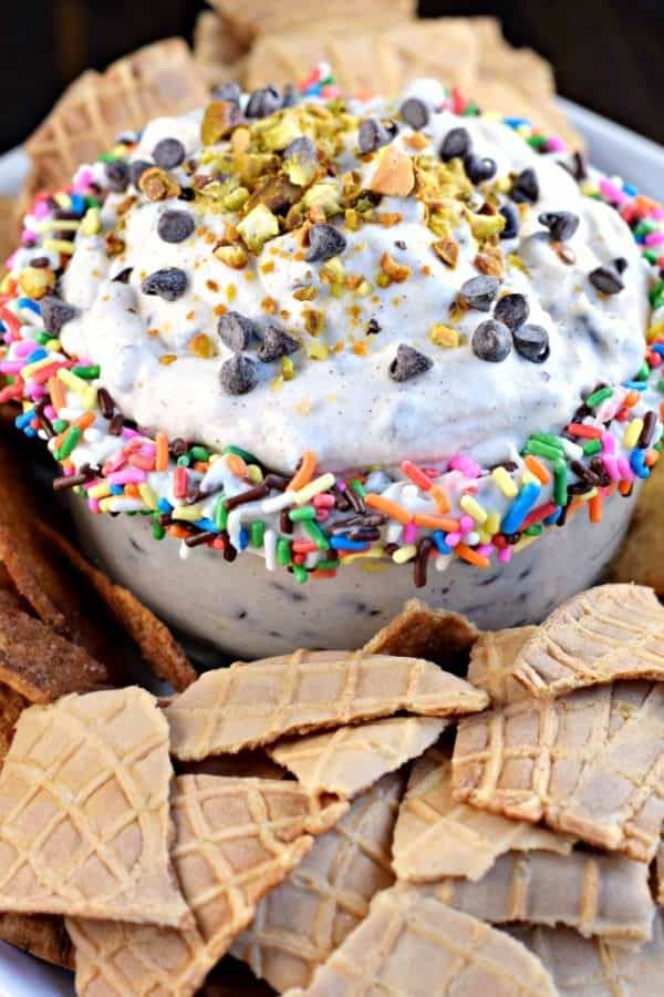 Cannoli dip with sprinkles, pistachios, and chocolate chips. Served on a platter of waffle cone pieces.