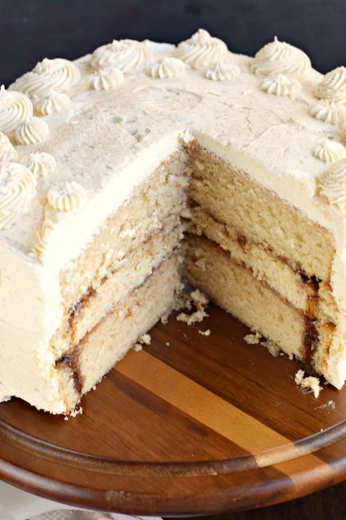 Cinnamon cheesecake cake on a wooden cake platter with a slice removed.