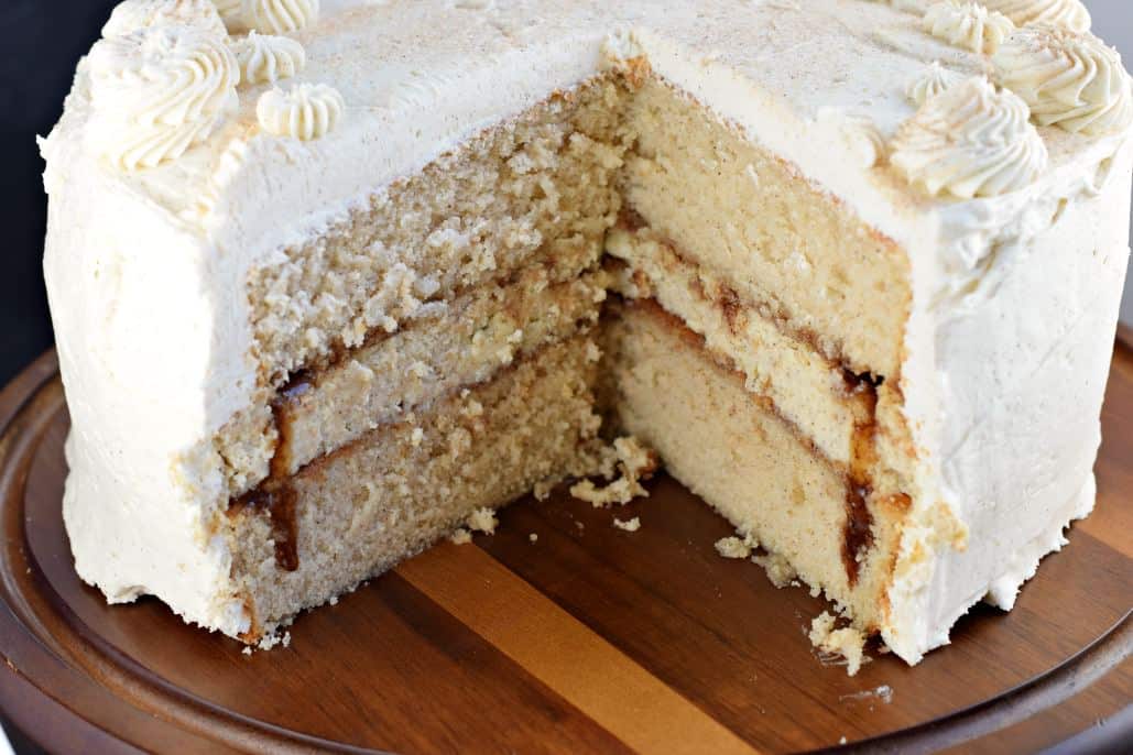Whole cinnamon cake with a slice removed on a wooden cake platter.