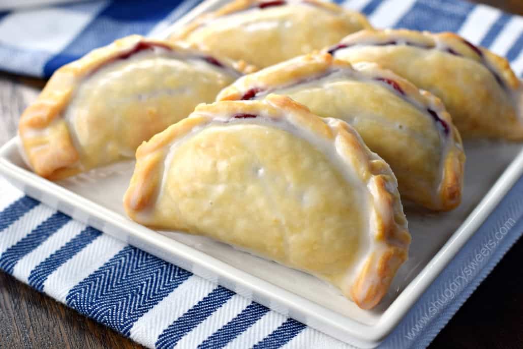 Hand pies filled with blueberry pie filling on a white plate with blue and white striped linen.