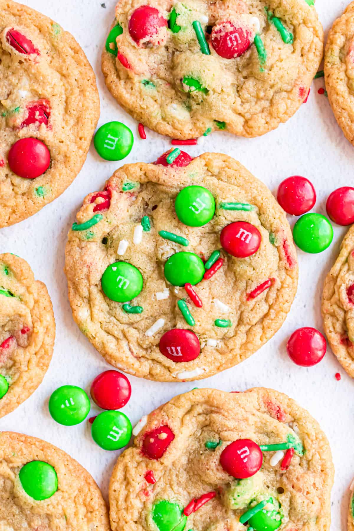 Baked M&M cookies with Christmas sprinkles on parchment paper.