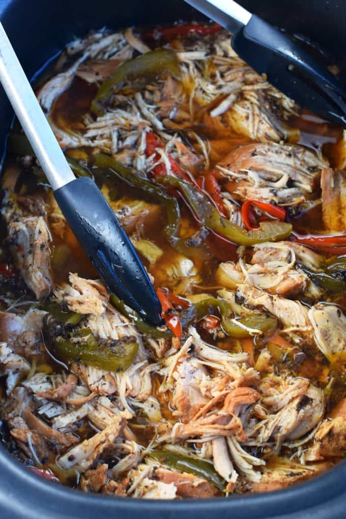 Tongs picking up shredded chicken and sliced peppers out of a crockpot.