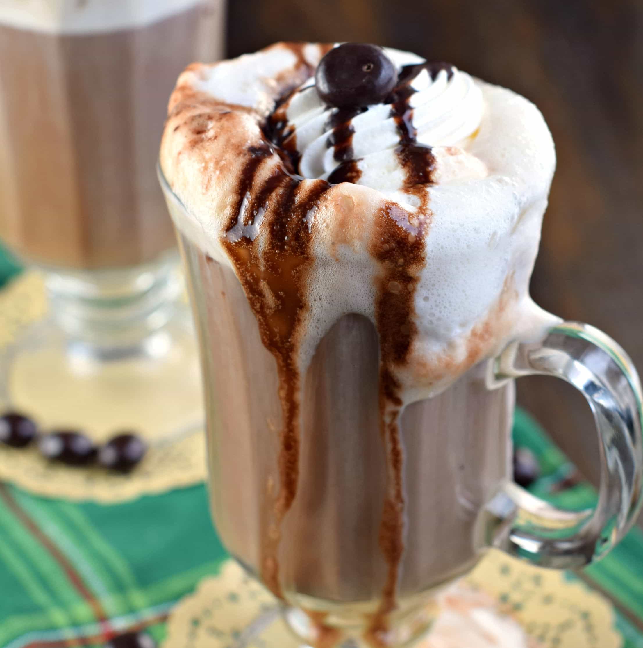 Hot mocha latte in a clear glass mug topped with whipped cream and chocolate sauce.