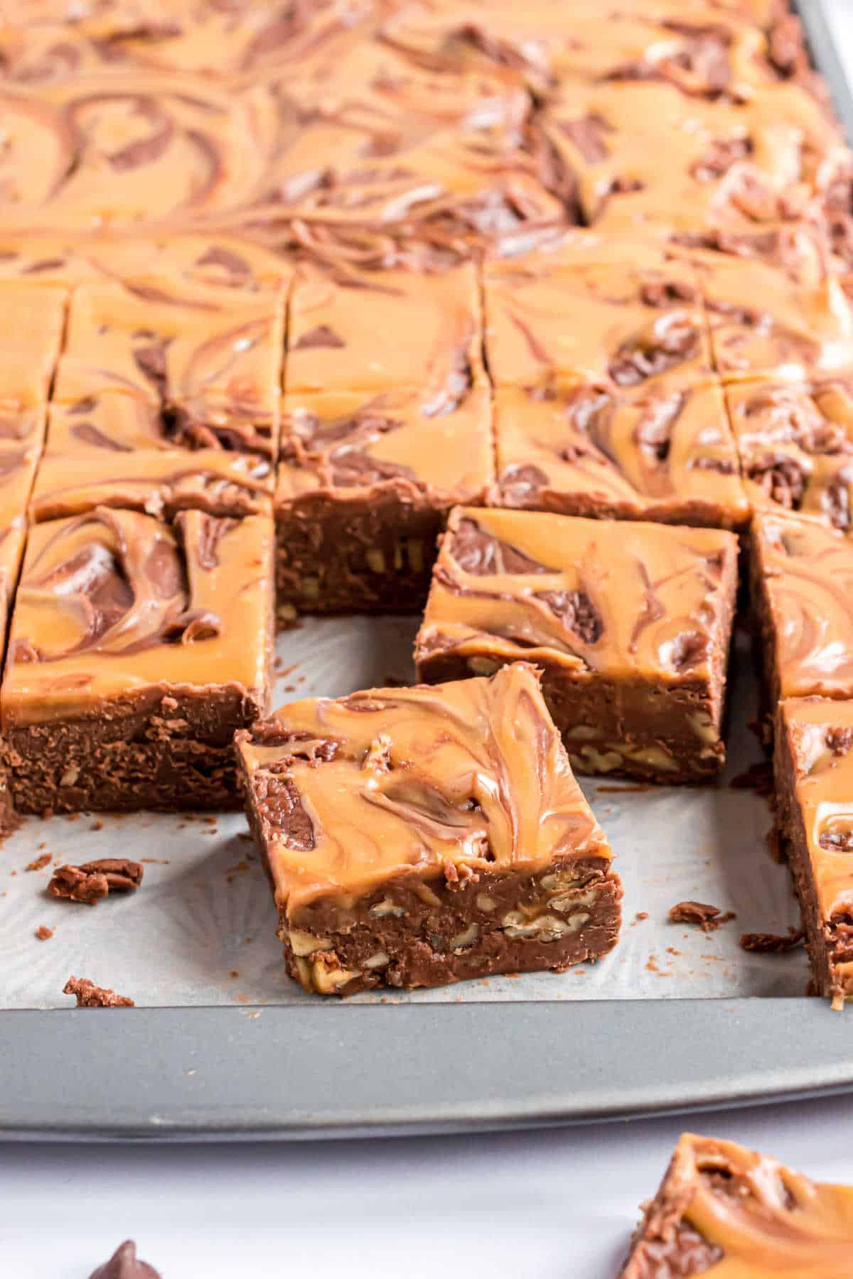 Pieces of chocolate caramel fudge on a cookie sheet cut into squares.