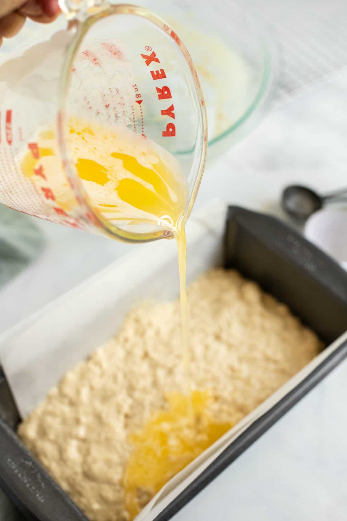 Melted butter being drizzled over uncooked beer bread batter in a loaf pan.