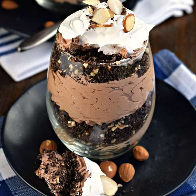 Stemless wine glass with layers of chocolate cookie crumbs, chocolate cheesecake, almonds, and whipped cream.