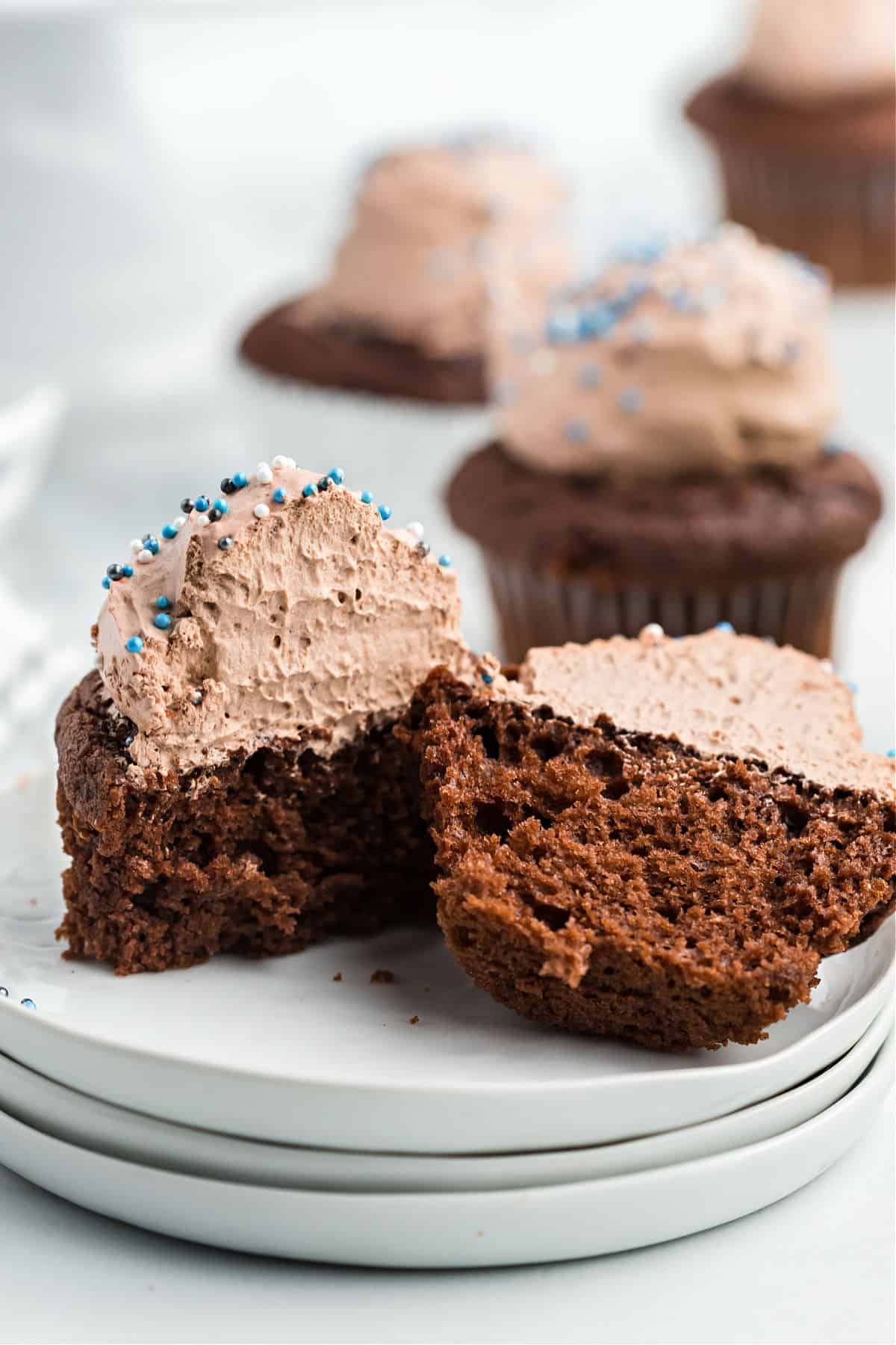 Chocolate frosted cupcake cut in half on a white plate.