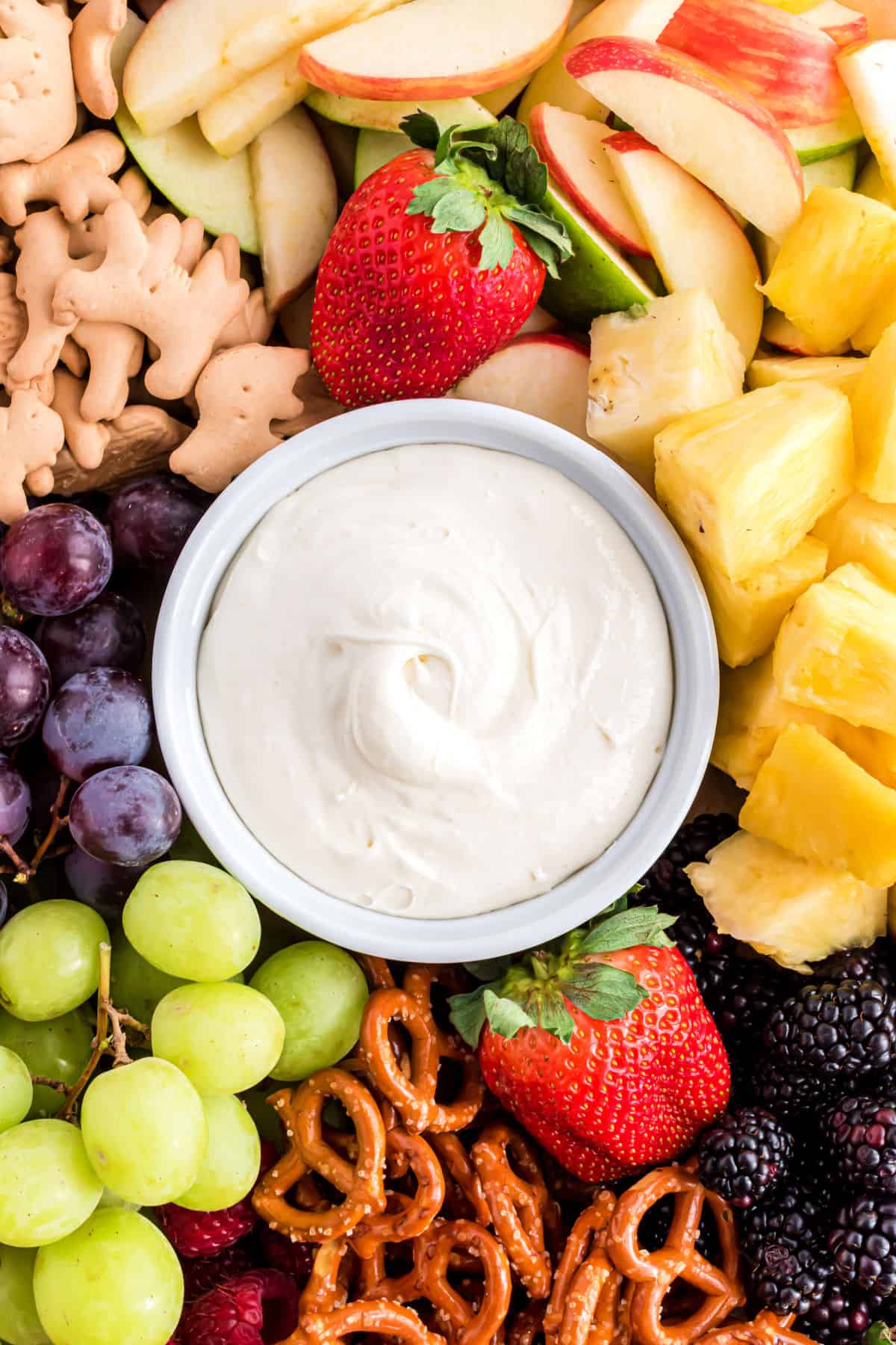 Fruit dip on a serving platter filled with fruit, cookies, and pretzels.