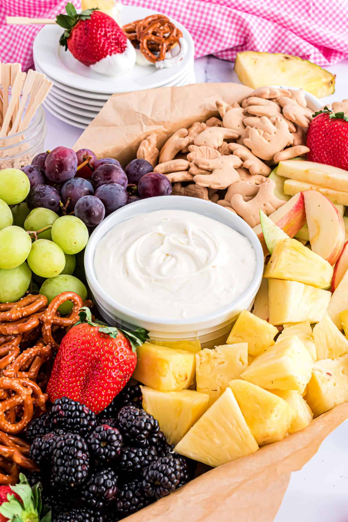 Cream cheese fruit dip served with fresh fruits, cookies, and pretzels on a wooden serving tray.