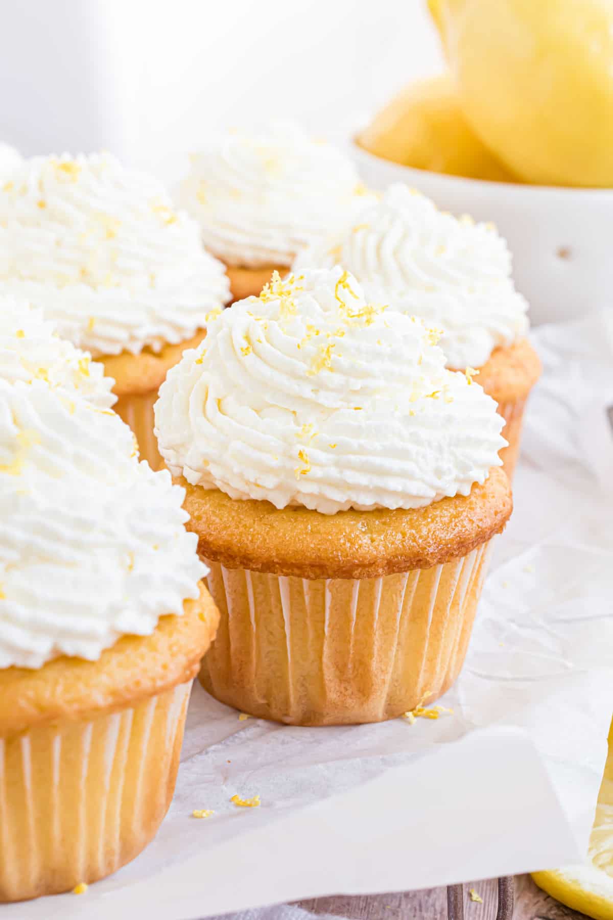 Cupcakes with lemon whipped cream on top on a white plate with parchment paper.