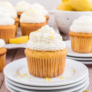 Cupcake with lemon frosting on a stack of white plates.