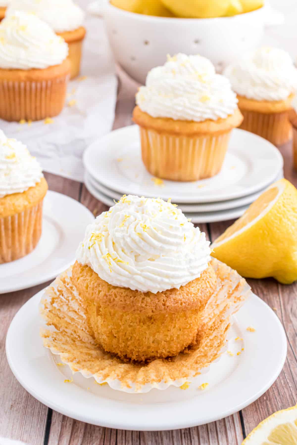 Lemon cupcake with lemon whipped cream on a white plate with wrapped taken off.