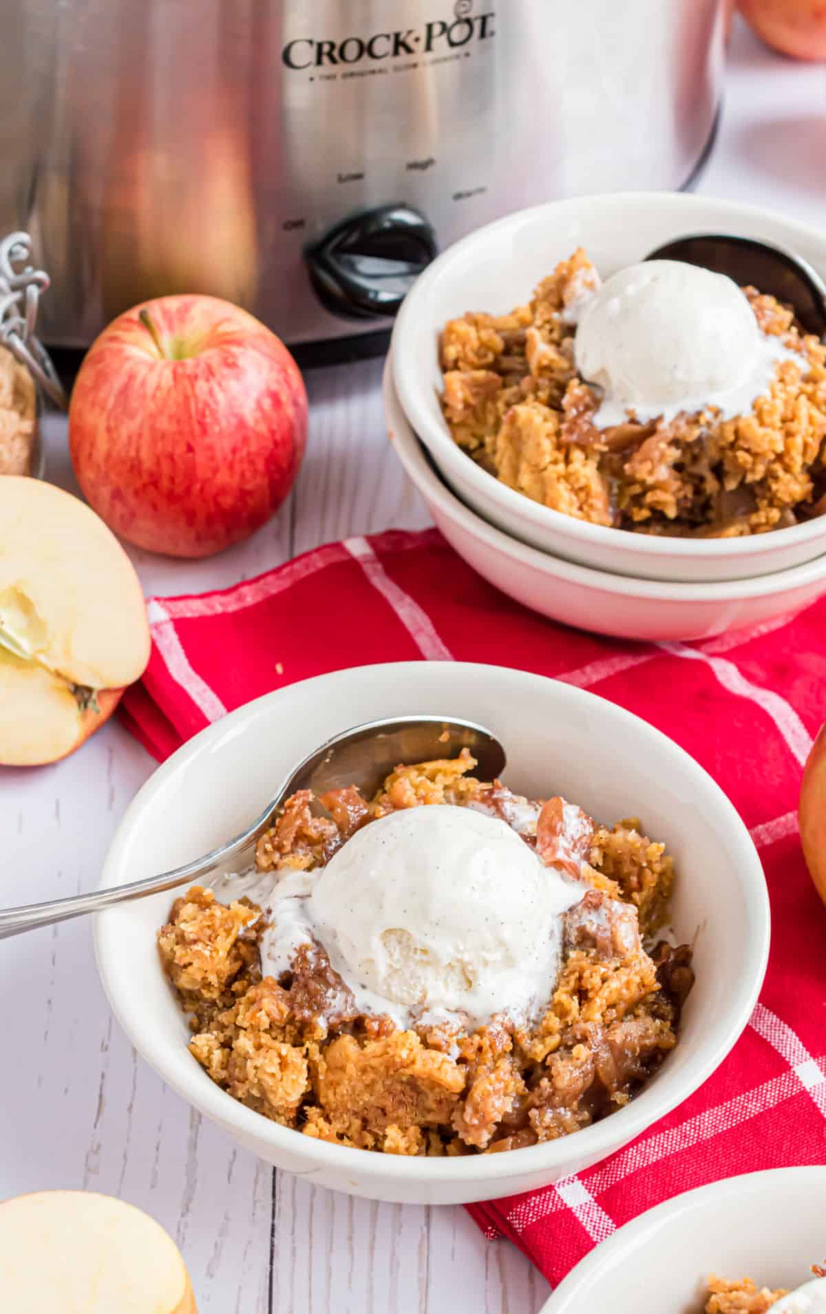 Apple cake in a white bowl topped with vanilla ice cream.