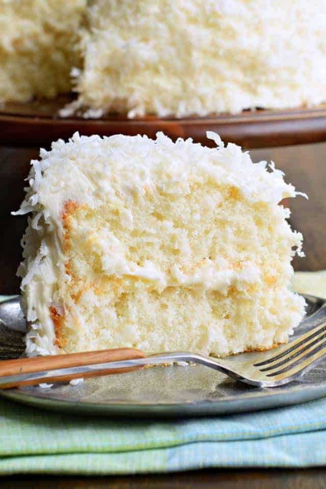 Moist slice of coconut cake on a silver plate with a fork.