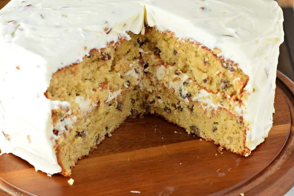 Italian cream cake on a wooden cake plate with a slice removed.