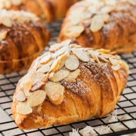 A close-up of easy almond croissants topped with sliced almonds and powdered sugar on a cooling rack.