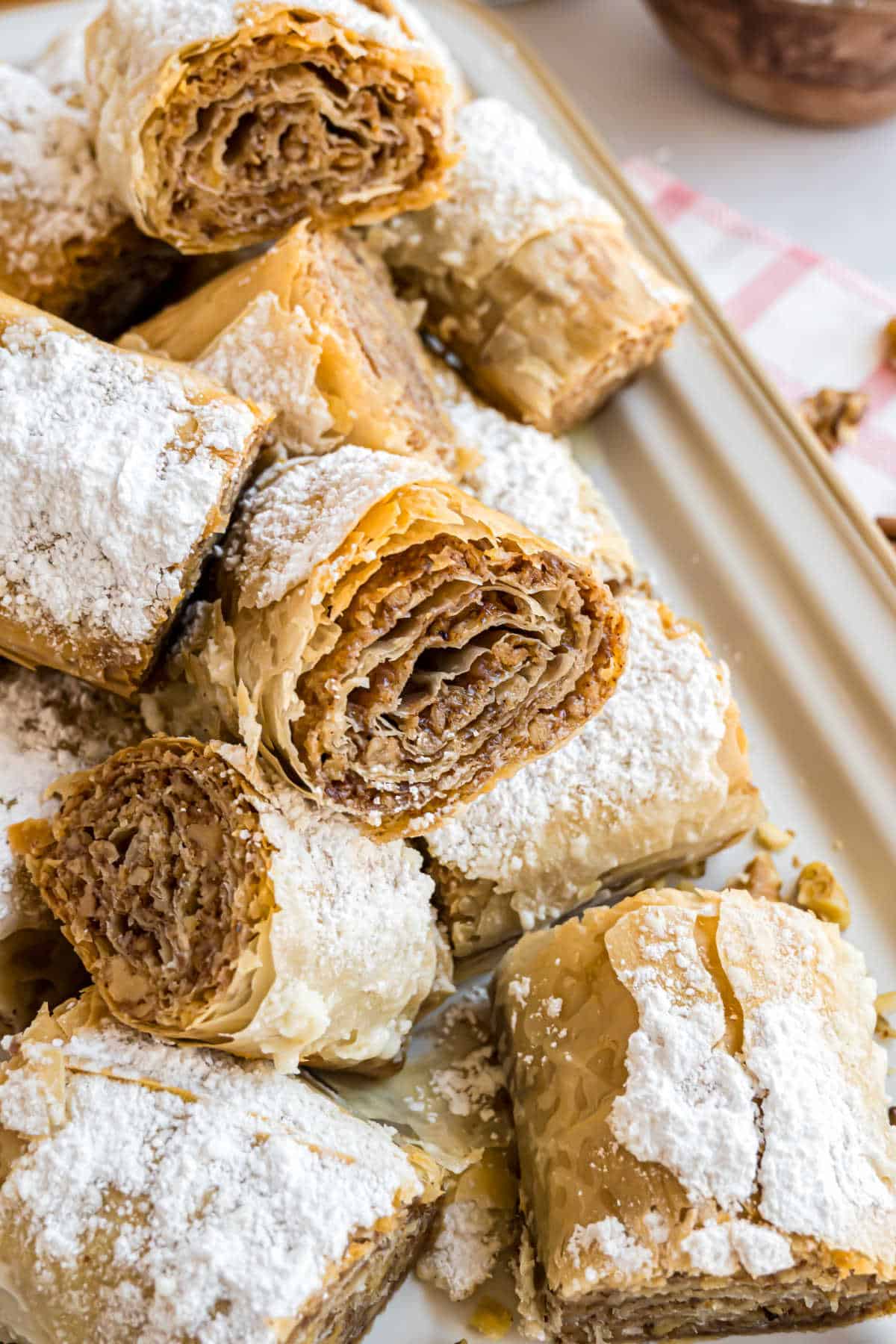 Slices of flaky baklava dusted with powdered sugar are artfully arranged on a serving tray.