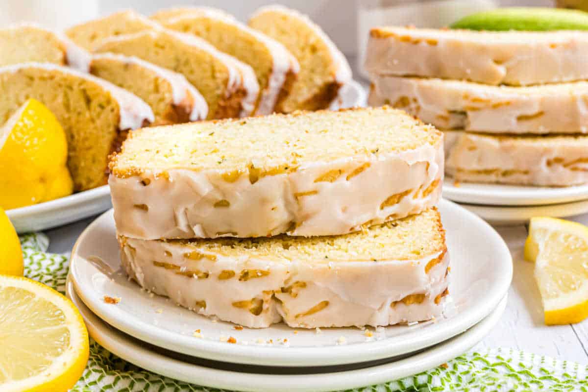 Two slices of lemon zucchini bread on a plate, with more slices and lemon wedges in the background.