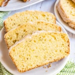 Three slices of glazed lemon zucchini bread on a white plate, showcasing a moist and airy texture.