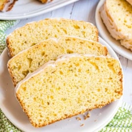 Three slices of glazed lemon zucchini bread on a white plate, showcasing a moist and airy texture.